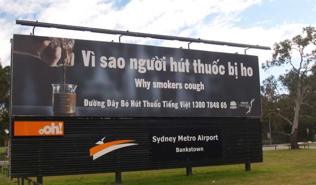 A dohányzás veszélyeire figyelmeztető angol és vietnámi nyelvű óriásplakát Sydney-ben. A kelet-ázsiaiak között sokkal elterjedtebb a dohányzás, mint az ausztrál népességben általában, ezért kell számukra külön is kihangsúlyozni, hogy a dohányosok azért köhögnek, mert ennyi kátrány van a tüdejükben.